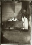 Woman standing next to a table with dishes. EW Carter photo ca. 1900 Glass negative: 5″x7″