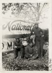 1909 NATIONAL Vanderbilt Cup Races Men posing in front of National banner Louis Disbrow, Al Livingston, Johnny Aitken photo Burton Historical Collection Detroit Public Library